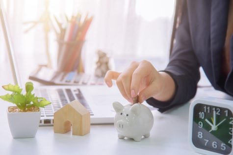 Coins on hand are dropped Piggy bank on wooden top table, money savings concept